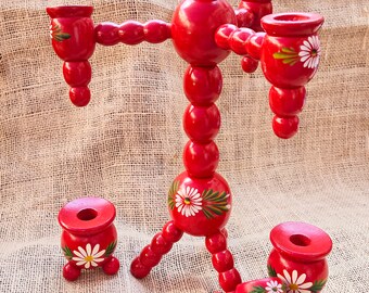 May include: A set of red wooden candle holders with white daisy designs. The set includes a large candelabra with four candle holders and four smaller individual candle holders.