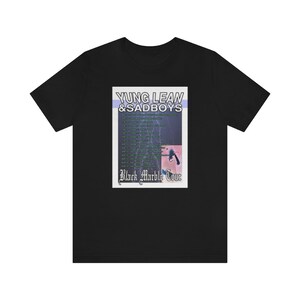 May include: Black t-shirt featuring a graphic print of a concert poster for Yung Lean & Sadboys Black Marble Tour. The poster has a blue and purple background with a lightning bolt design and text in white.