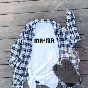 May include: White t-shirt with the text "MAMA" in black letters with a gold lightning bolt in between the words.