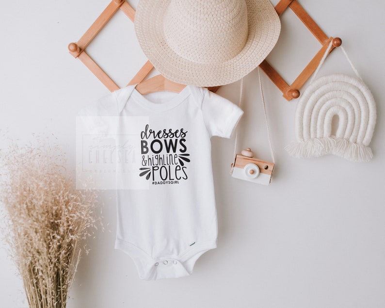 May include: White baby onesie with black text that reads "dresses bows & high line poles #daddysgirl"