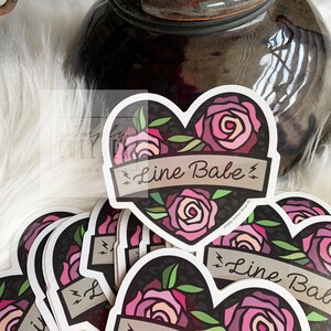 Pu&ograve; includere: Un mucchio di adesivi a forma di cuore con uno sfondo a stampa leopardo bianco e nero. Gli adesivi presentano rose rosa e uno striscione che recita "Line Babe" con fulmini su entrambi i lati.