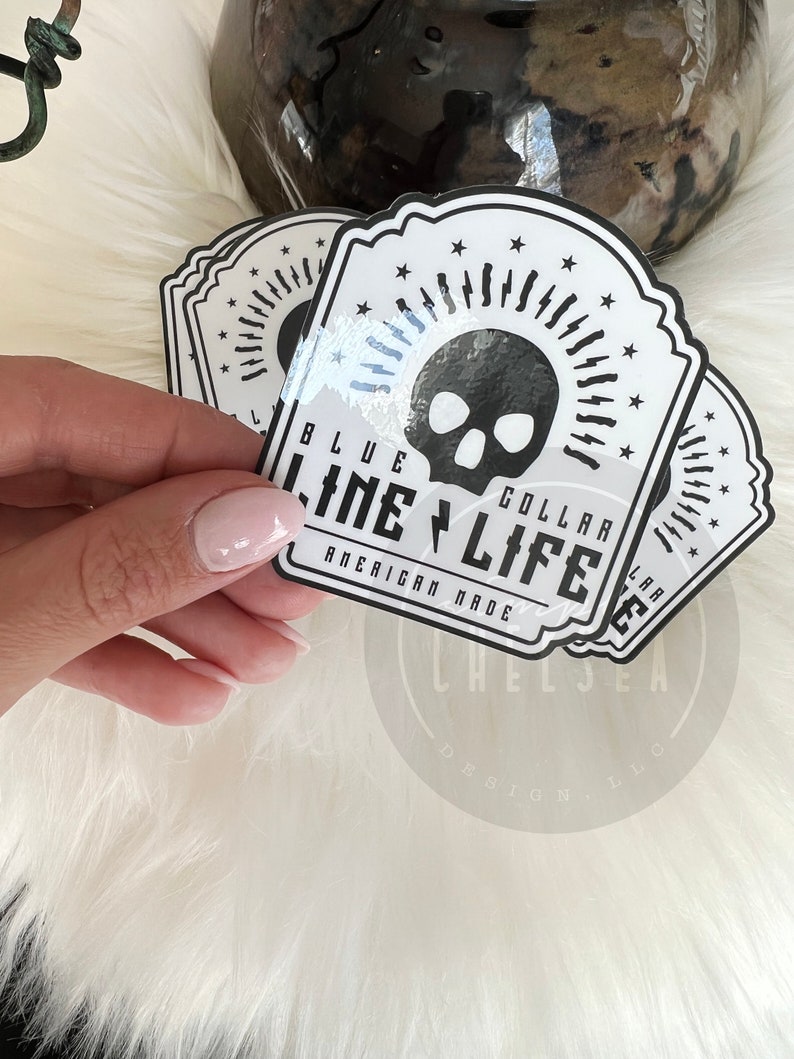 Pu&ograve; includere: Un adesivo bianco con un teschio nero e il testo "Blue Collar Life American Made" in un font in stile vintage.