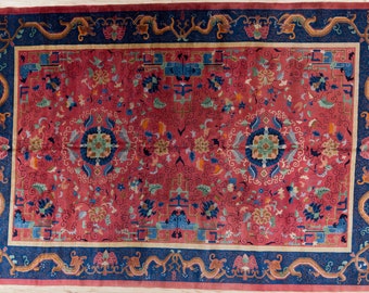May include: A red rug with a blue border and intricate floral patterns. The rug features a central design with a circular motif and a repeating pattern of stylised flowers and leaves.