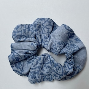 Peut inclure: Un chouchou bleu avec un motif floral. Le tissu est bleu clair avec un motif floral bleu plus foncé. Le chouchou est froncé et a un aspect doux et texturé. Cet accessoire pour cheveux est parfait pour ajouter une touche de style à n'importe quelle coiffure.