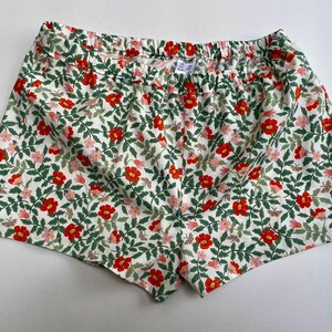 May include: White cotton shorts with a floral print featuring red and pink flowers and green leaves.