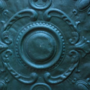 May include: A teal blue decorative ceiling tile with a raised, circular design in the center. The tile has a textured, ornate pattern around the edges.