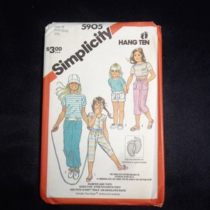 May include: Simplicity Hang Ten sewing pattern envelope featuring illustrations of girls in various outfits. The envelope is white with red and black text, including the price and size. The pattern includes instructions for making rompers and tops.