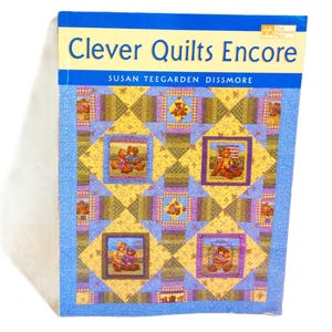 May include: A book titled "Clever Quilts Encore" by Susan Teegarden Dissmore. The cover features a quilt design with yellow, blue, and purple squares, and teddy bear illustrations. The book has a blue border and a white background.