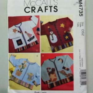 May include: A McCall's Crafts pattern envelope featuring four sweater designs. Each sweater is a different color and decorated with various appliqués, including stars, a snowman, and flowers. The envelope has the text "McCall's Crafts" at the top.