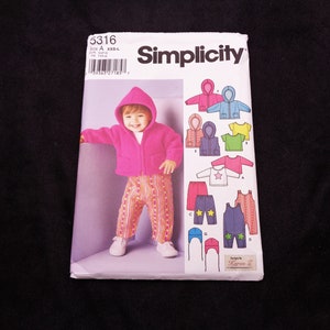 May include: Simplicity sewing pattern 5316 for children's clothing. The pattern features a child wearing a pink hooded jacket and striped pants. Other clothing options include a star-decorated shirt and overalls. The pattern includes the Simplicity logo.