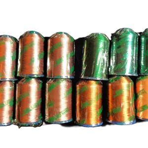 May include: A collection of spools of thread in shades of orange and green. The thread is wrapped in clear plastic with green and white labels. The spools are stacked in rows, creating a visually appealing display.