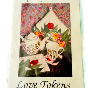 May include: A packaged tea set with a ladybug theme. The image shows a teapot, teacup, and quilted items with ladybug and floral designs. The text "Lady-Bug Tea Set" and "Love Tokens" are visible.