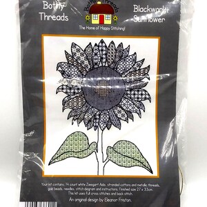 May include: A blackwork sunflower cross-stitch kit in a clear plastic package. The design features a detailed sunflower with intricate patterns in shades of gray and black. The kit includes the Bothy Threads logo and the text "Blackwork Sunflower". The finished size is 27 x 33 cm.