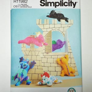 May include: Simplicity sewing pattern featuring a castle and colorful dragon plushies. The pattern includes a variety of dragon designs in shades of pink, blue, yellow, purple, and black. The pattern is one size and designed and printed in the USA.
