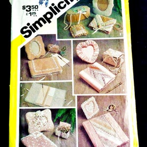 May include: Simplicity pattern envelope featuring various craft projects. The projects include a heart-shaped pillow, a picture frame, and a small box, all with lace and ribbon details. The envelope is yellow and white with the number 5296.