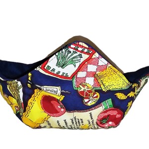 May include: A fabric bowl cozy with a navy blue interior and a colorful exterior featuring Italian food imagery. The design includes tomatoes, pasta, and the word "BASIL" on a white background with red checkered patterns.