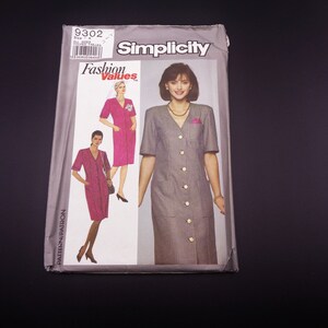 May include: Simplicity sewing pattern envelope featuring a dress design. The envelope displays a woman in a gray and white checked dress with large buttons and a pocket. The words "Fashion Values" and "Simplicity" are visible.