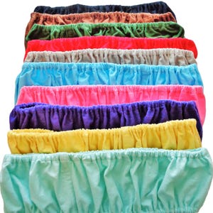 May include: A stack of colorful, elastic waistbands in various shades, including navy, brown, green, red, gray, light blue, pink, purple, yellow, and mint green. The fabric appears to be soft and gathered, with a simple, casual design.