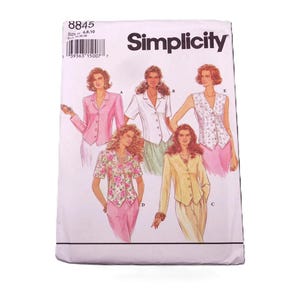 May include: A Simplicity sewing pattern envelope featuring illustrations of women's suit and blouse designs. The envelope is white with the brand name "Simplicity" in black. The designs include a pink suit, a white blouse, and a floral top.
