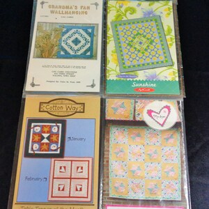 May include: Four packaged quilt patterns. The top left package reads "Grandma's Fan Wallhanging." The top right package is labeled "Sunshine." The bottom left package is labeled "Cotton Way Table Topper of the Month." The bottom right package is labeled "Sweet as Pie #2342."