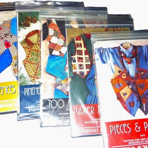 May include: A collection of sewing patterns for vests and other garments, sealed in clear plastic bags. The patterns feature colorful patchwork designs and include text such as "Pieces & Patches" and "Fences".
