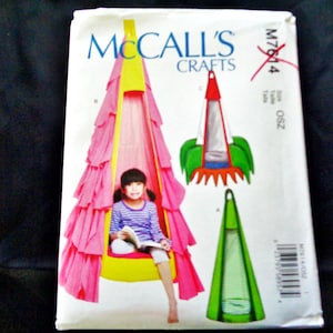 May include: McCall's Crafts sewing pattern for a child's hanging tent. The pattern shows a pink, yellow, and white tent with a child sitting inside. Additional tent designs are shown in green, red, and white. The pattern is on a white background.