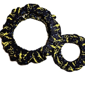 May include: A navy blue fabric hair accessory with a yellow scissors pattern and small blue dots. The accessory has two connected circular shapes, one larger and one smaller, with a ruffled edge.