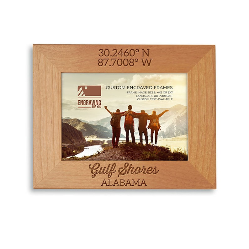 May include: A wooden picture frame with a photo of a group of people standing on a mountain overlooking a lake. The frame is engraved with the text "Gulf Shores, Alabama" and the coordinates "30.2460&deg; N 87.7008&deg; W".