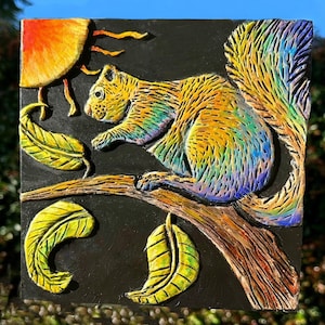 May include: A colorful, iridescent squirrel sculpture on a black background with yellow leaves. The squirrel is perched on a branch with its tail curled up behind it. The sculpture is made of a textured material and has a realistic appearance.
