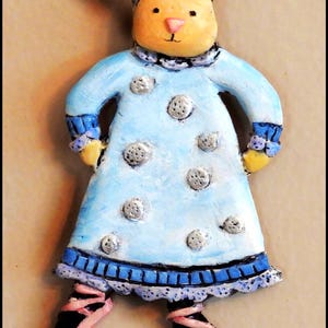 May include: A ceramic bunny figurine wearing a blue dress with white polka dots and pink ballet shoes.