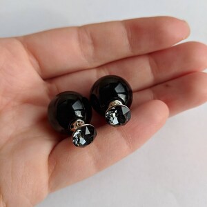 Puede incluir: Un par de pendientes de bot&oacute;n negros de doble cara. Cada pendiente presenta una esfera negra grande y brillante combinada con un cristal gris facetado m&aacute;s peque&ntilde;o. Los pendientes est&aacute;n engarzados en postes plateados.