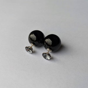 Puede incluir: Un par de pendientes esf&eacute;ricos negros y brillantes. Cada pendiente presenta una esfera negra grande y un cristal facetado plateado m&aacute;s peque&ntilde;o. Los pendientes se muestran sobre un fondo blanco liso.