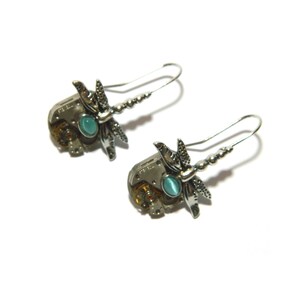 May include: Steampunk-style earrings featuring a dragonfly design. The earrings have a silver finish with intricate details, including gears and a teal-colored stone. The dragonfly wings are detailed and add a unique touch.
