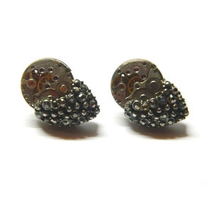 Puede incluir: Un par de pendientes de plata con un pequeño racimo de piedras preciosas negras en forma de lágrima y un mecanismo de reloj circular en el centro.