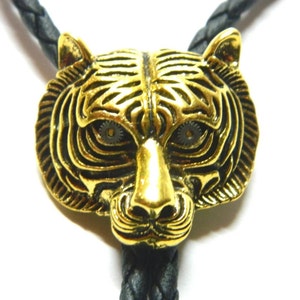 May include: A gold-coloured tiger head bolo tie with black braided leather cord. The tiger's eyes are made of metal gears.