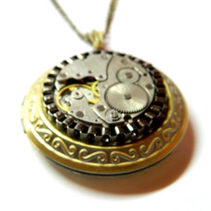 May include: A steampunk-style pendant necklace featuring a circular locket with intricate watch gears visible inside. The locket has a gold-colored frame with a decorative scroll design. The necklace chain is a thin, gold-colored metal.
