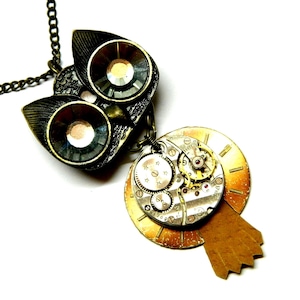 May include: A bronze owl pendant necklace with crystal eyes and a steampunk-style clock face charm. The clock face is made of metal and has a brown leather accent.