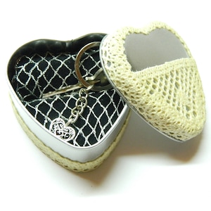 May include: A silver heart-shaped trinket box with a crocheted lid. The box is open and contains a silver key chain with a heart charm.