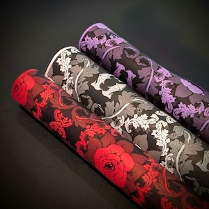 May include: Three rolls of decorative wrapping paper with floral patterns. The paper is black with white and gray floral designs. The top roll is purple, the middle roll is white, and the bottom roll is red.