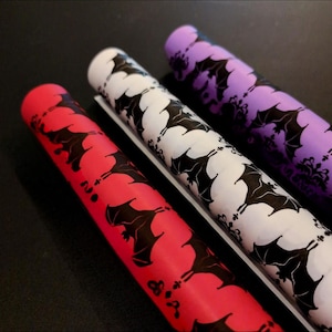 May include: Three rolls of wrapping paper with a black bat pattern. The rolls are red, white, and purple.