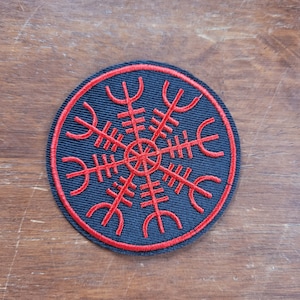 Op de afbeelding: Een zwarte ronde patch met een rood geborduurd Vegvisir-symbool. Het symbool is een Noorse richtingswijzer, vaak geassocieerd met bescherming en begeleiding.