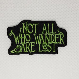 Puede incluir: Parche bordado verde sobre fondo negro con el texto "Not all who wander are lost."