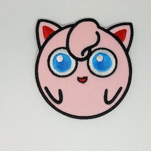 May include: Pink and white embroidered patch of a cartoon character with blue eyes and a red nose. The character is a pink, round creature with a curled tail.