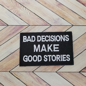 Pode incluir: Etiqueta bordada preta com texto branco que diz "Bad Decisions Make Good Stories".