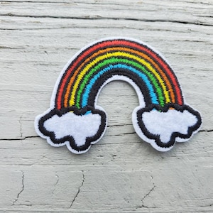 May include: An embroidered patch featuring a rainbow with white clouds on either side. The rainbow has red, orange, yellow, green, blue, indigo, and violet stripes.