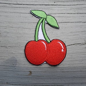 May include: A red and green embroidered cherry patch. The cherry is a classic fruit design.