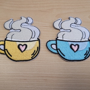 May include: Two embroidered iron-on patches of coffee mugs with steam and a pink heart. One mug is yellow and the other is blue.