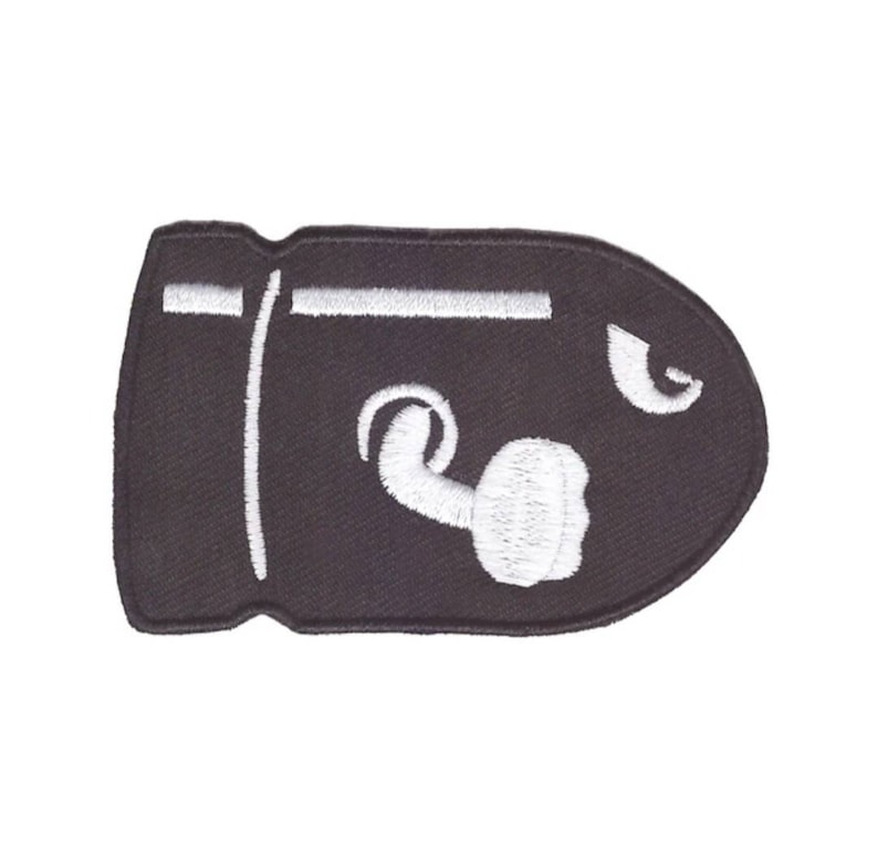 May include: A black embroidered patch in the shape of a bullet, featuring white details. The design includes a white exhaust cloud and a white line. This patch is suitable for jackets, bags, or other fabric items.