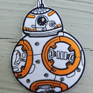 May include: White and orange embroidered patch of a Star Wars BB-8 droid. The patch is round and has a detailed design of the droid's head and body.