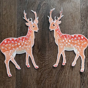 May include: Two embroidered iron-on patches of orange and white deer with white antlers. The deer are facing opposite directions.